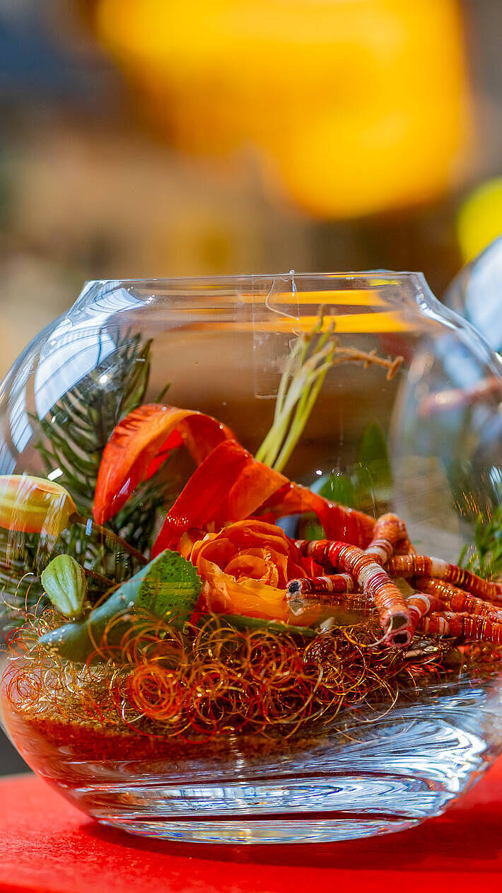 Farbenfrohe Glasdekoration in Rot-Orange mit winterlichen Akzenten, liebevoll arrangiert im JOSKA Glasparadies in Bodenmais.