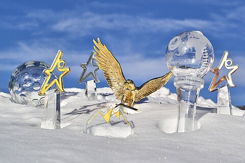 Glaspokale und Trophäen aus dem JOSKA Glasparadies im Schnee, darunter der Biathlon-Weltcup-Glaspokal und goldene Awards.