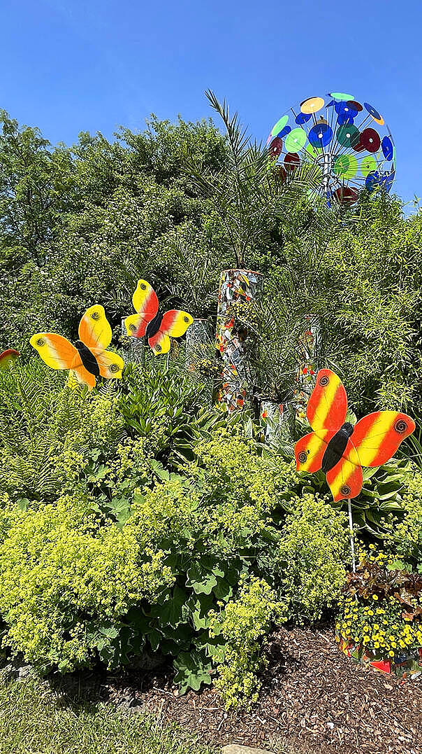 Bunte Fusingglas-Schmetterlinge als Gartenstecker vor üppiger Vegetation im JOSKA Glasparadies Bodenmais
